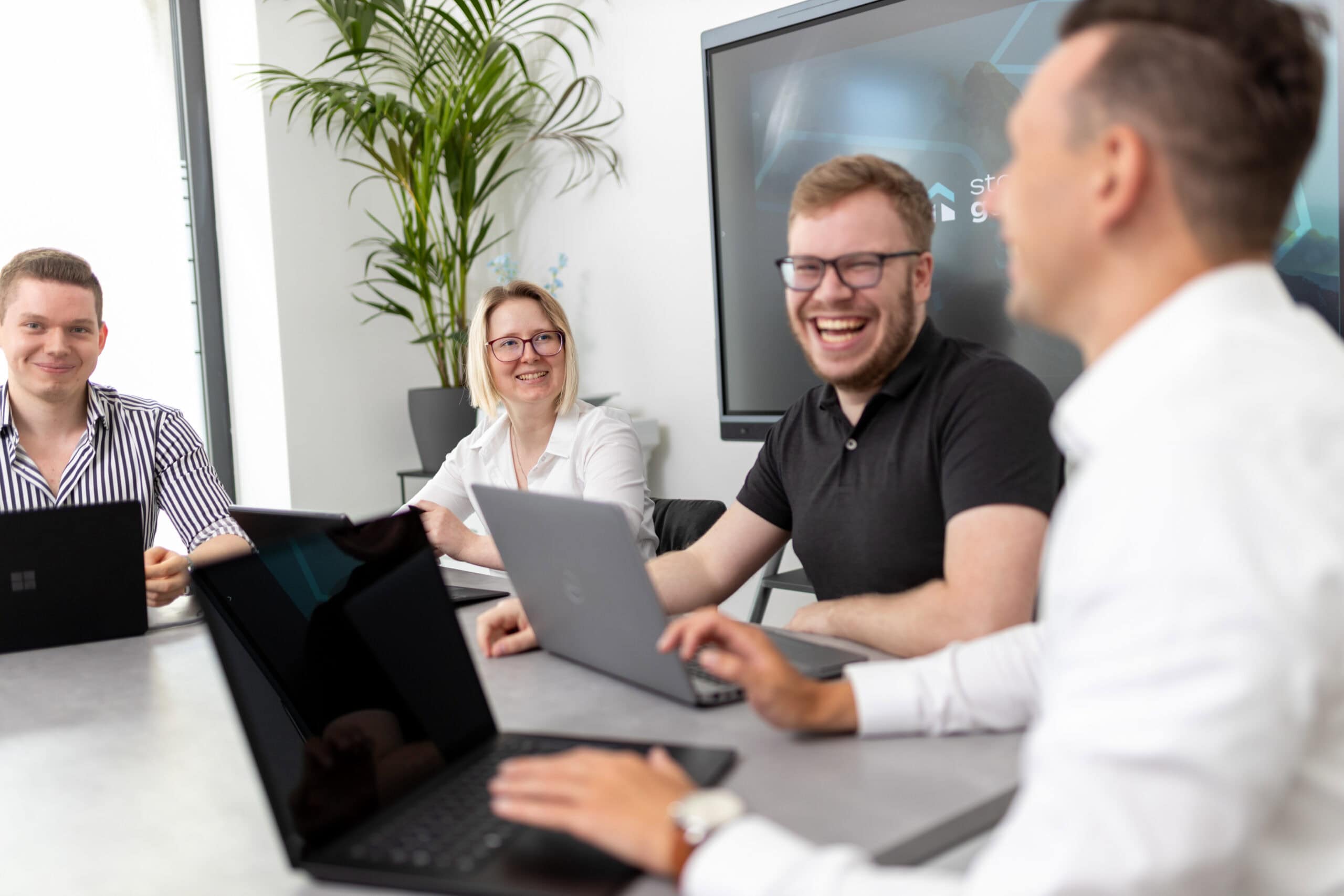 Gruppe von IT-Fachleuten lacht während einer entspannten Teambesprechung im modern ausgestatteten Konferenzraum